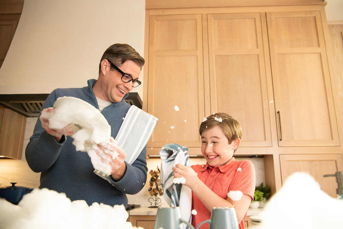 Man wears Echo Frames glasses while doing dishes with his young son