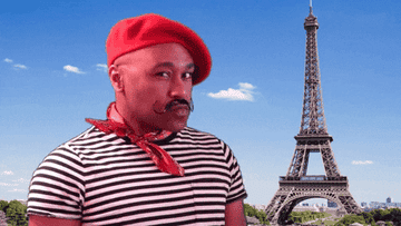 A French man n a beret stands in front of the eiffel tower