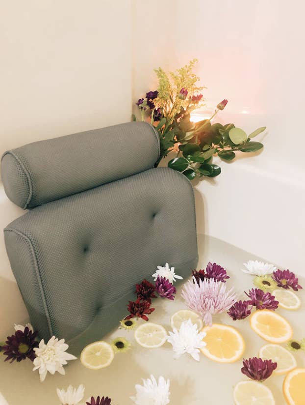 reviewer's ritual bath filled with flowers and sliced citrus with the back and neck pillow attached to the bathtub