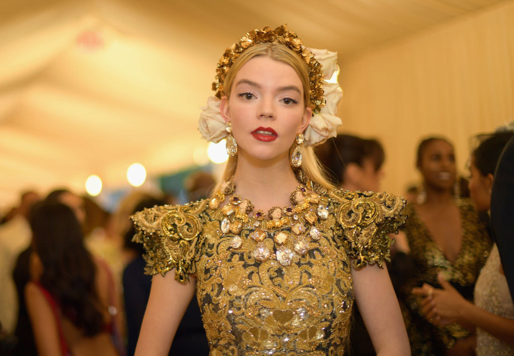 Anya at the Heavenly Bodies Met Gala wearing a golden flower crown, necklace with angel heads, and matching gold-patterned short-sleeve dress