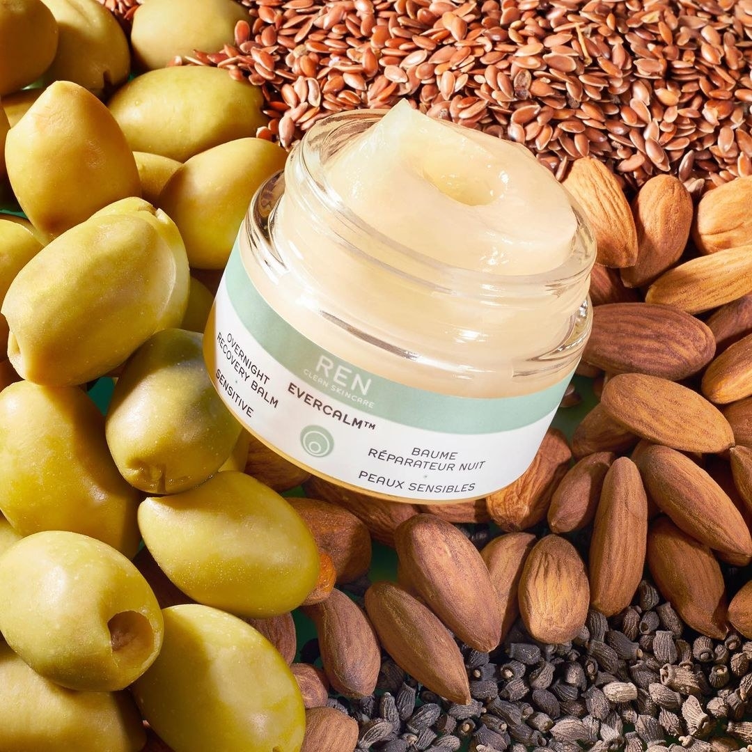 An open jar of the salve next to containers piles of fresh olives and almonds