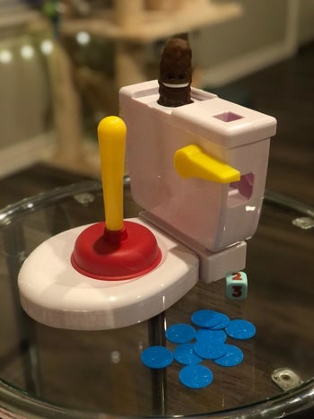 The toy toilet with a plunger, a plastic poop, some blue tokens, and a dice