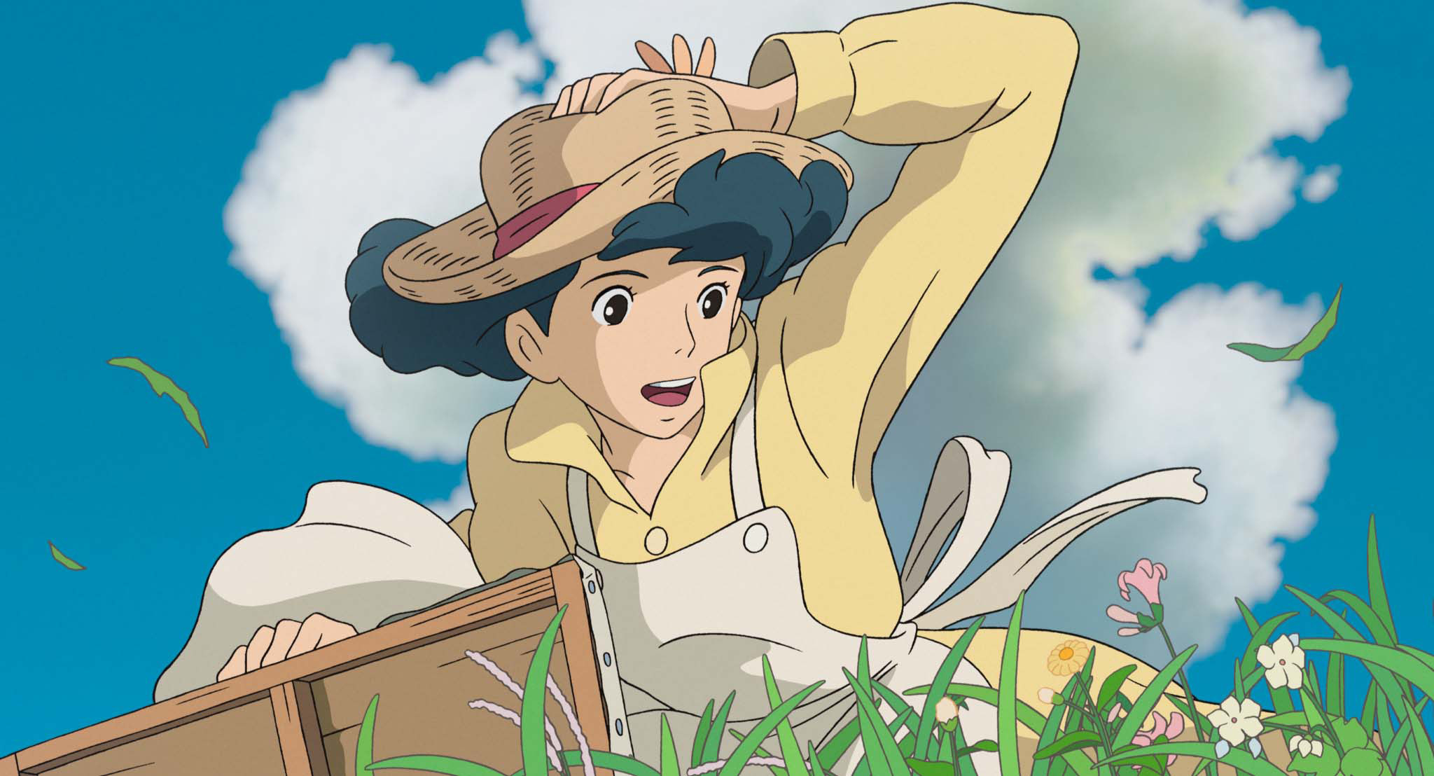 Naoko standing in some grass while holding her hat from blowing off her head