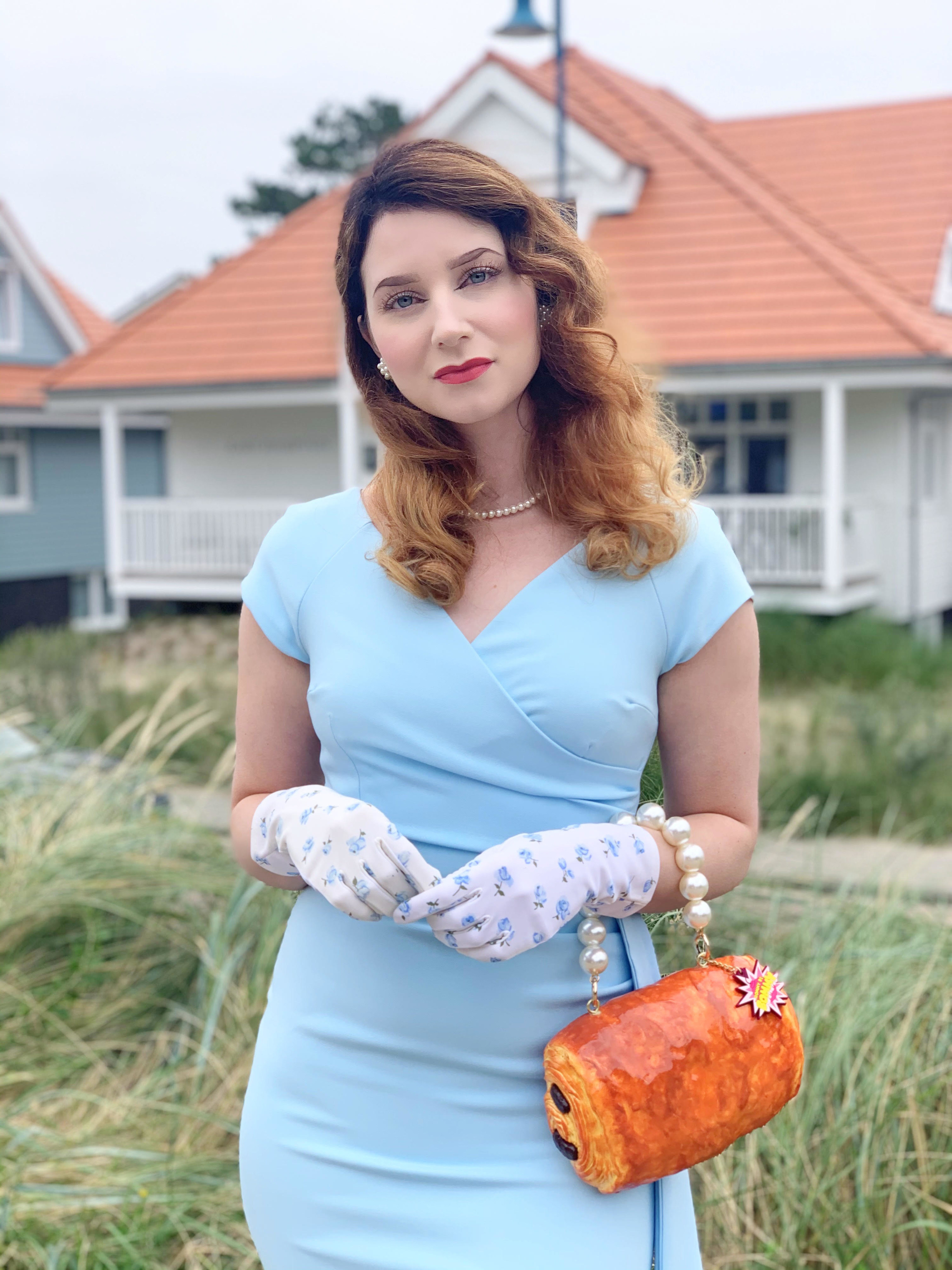 Rommy wears an elegant dress and gloves with a chocolate croissant purse