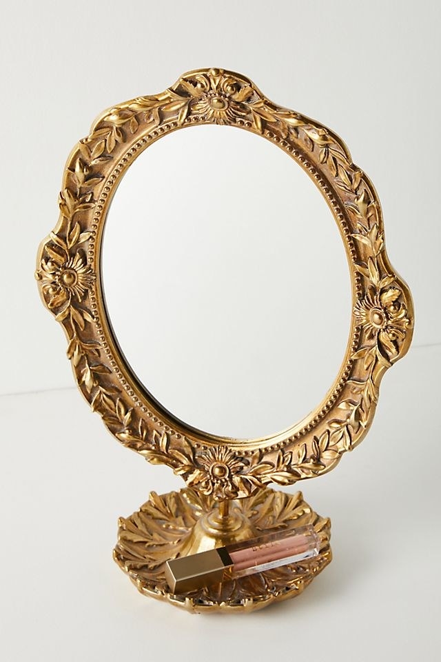 a bronze mirror with florals engraved around it and a dish attached to the bottom