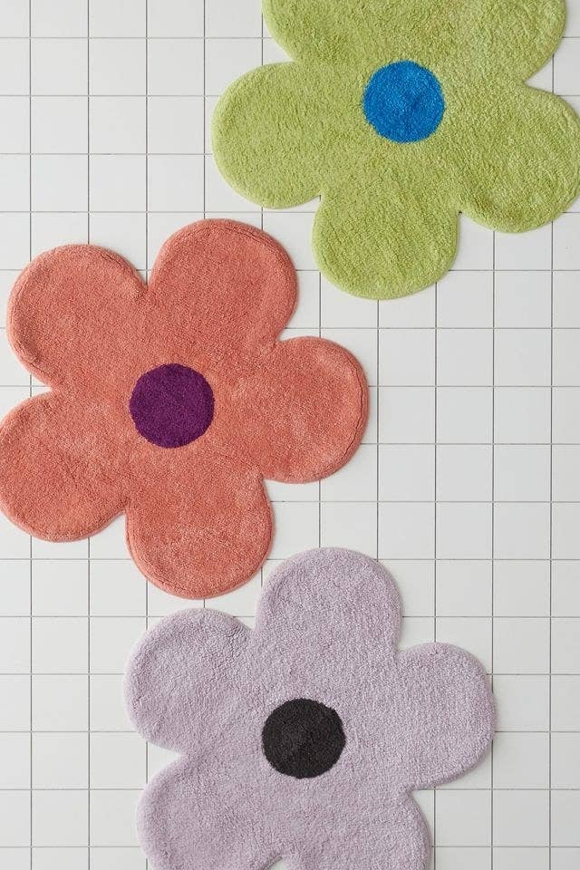 three flower shaped bath mats in pink, purple, and green