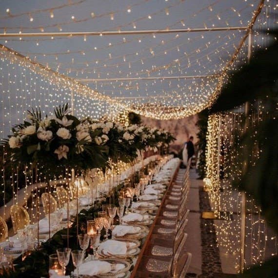 Product image of a canopy of warm string lights covering a long table set with tableware