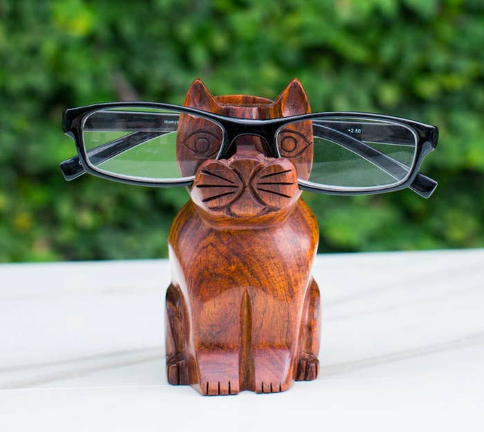 Dark brown wooden cat holding up black and yellow glasses