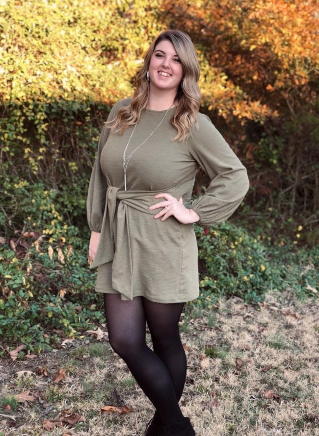 A reviewer wearing an army green long sleeve sweater dress with a twist tie