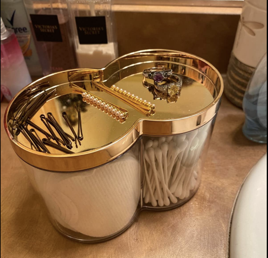 a reviewer photo of the canister with a gold lid containing cotton pads and swabs with hair accessories on top