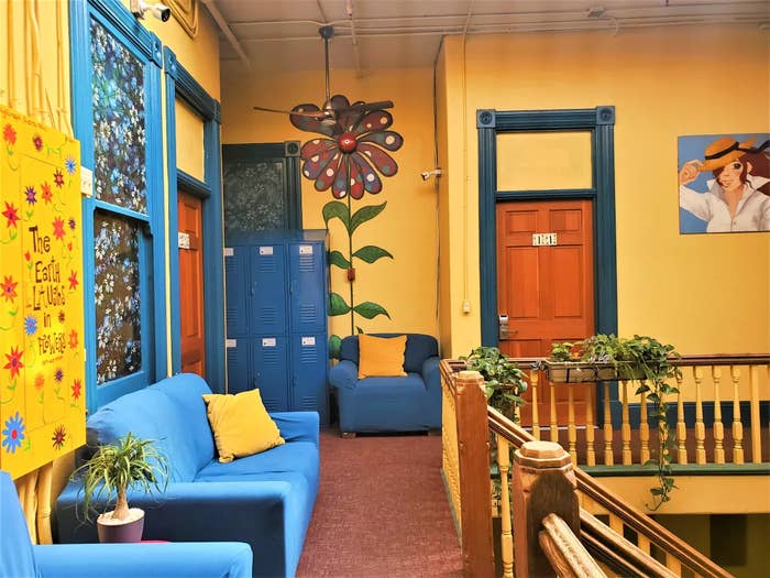 Hostel common area with couches, lockers, and a large staircase. Walls are filled with bright and fun flower murals.