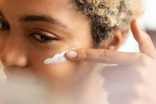 A woman spreads moisturizer on her face.