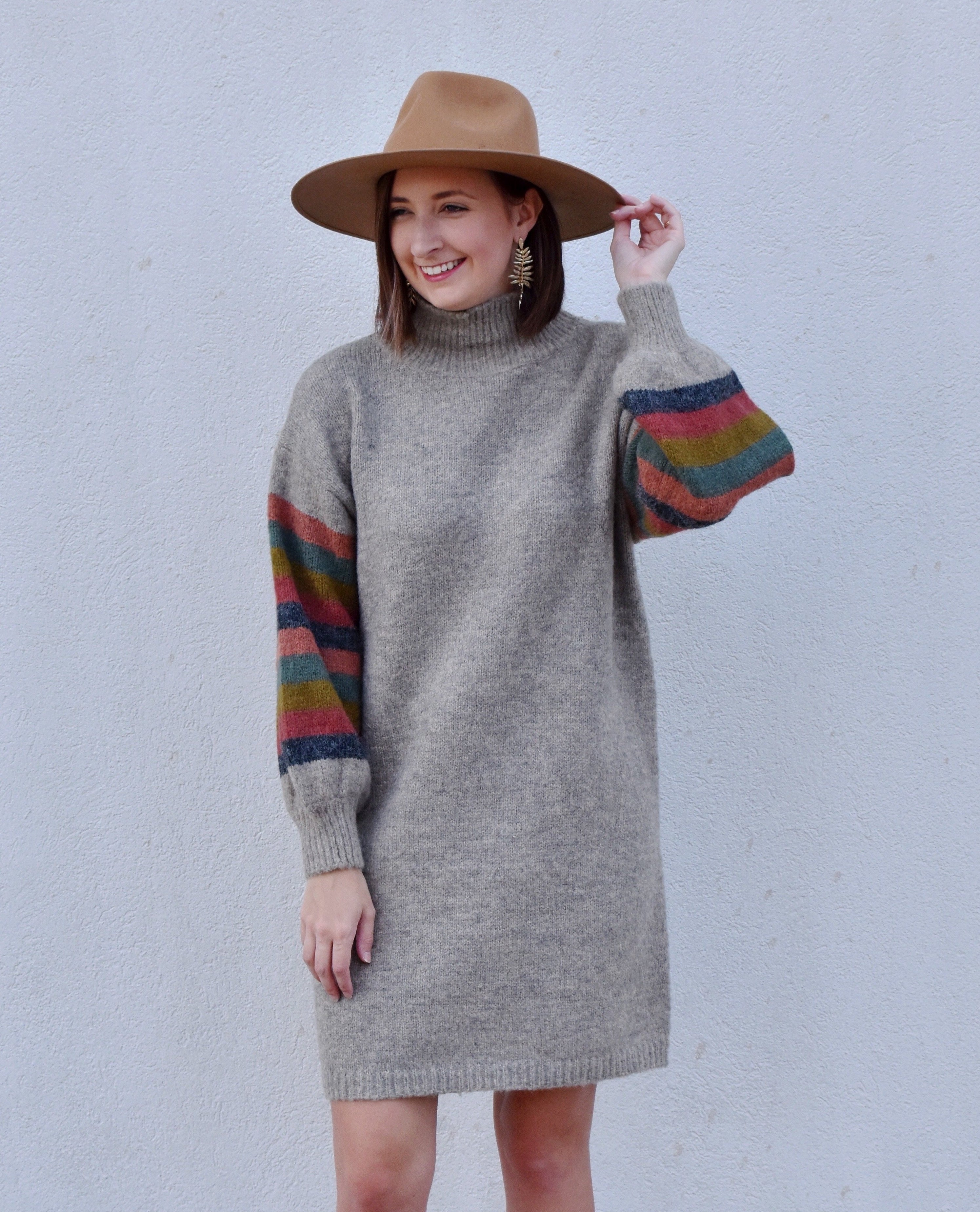 Model is wearing a grey sweater dress with multi-colored stripes on the sleeves