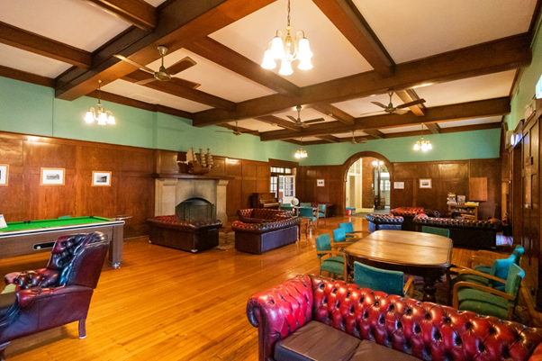 Hostel lounge with dark wood paneled walls, old vintage looking leather furniture, and a pool table