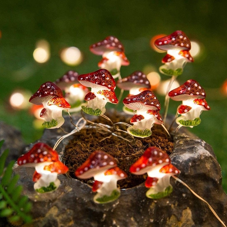Product image of red, white, and green mushroom-shaped lights on top of a tree stump
