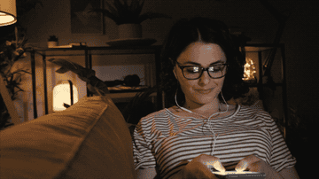 A woman is sitting on her couch, texting at night.