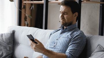 A visibly irritated man looks at a text message on his phone.