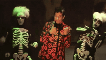 gif of david s pumpkins from snl pointing with his thumbs between his two dancing ghost sidekicks