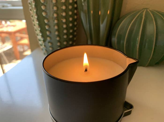 reviewer&#x27;s candle in black. the candle is lit and the shape has a small knotch for pouring the hot wax.