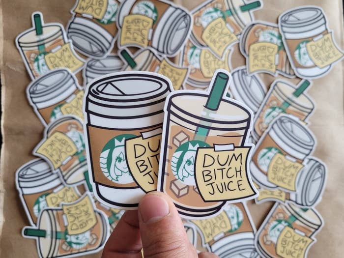 A person holding both the hot and iced coffee version of the sticker that says, "Dum Bitch Juice"