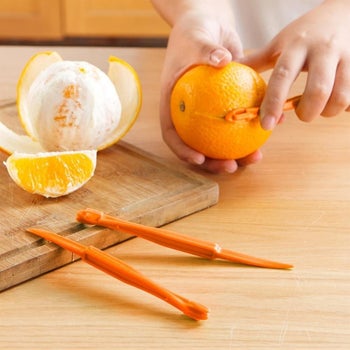 hand using the orange slicing tool to slice an orange