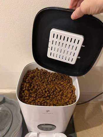 Reviewer pic of a view of the top of the automatic cat feeder, where a bunch of dry kibble is pre-loaded
