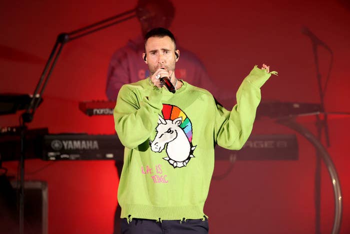 Adam performing at the Hollywood bowl, he wears a lime green sweater with a unicorn painted on it and the words &quot;LA is toxic&quot; in all caps
