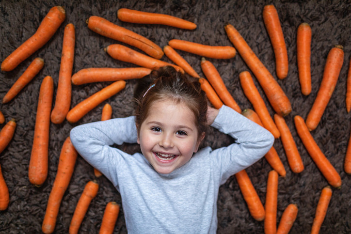 Joyful girl laying on her back in a field of carrots