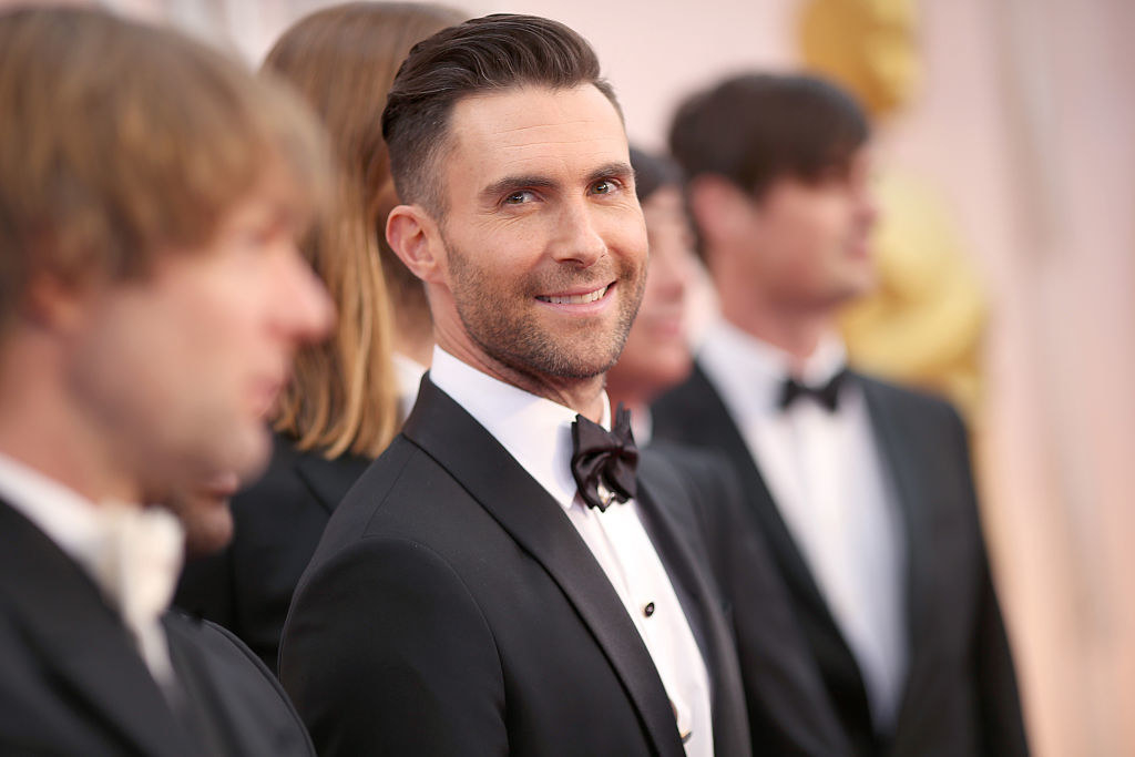 Adam at the Oscars, he gazes at the camera and wears a tux with a bowtie