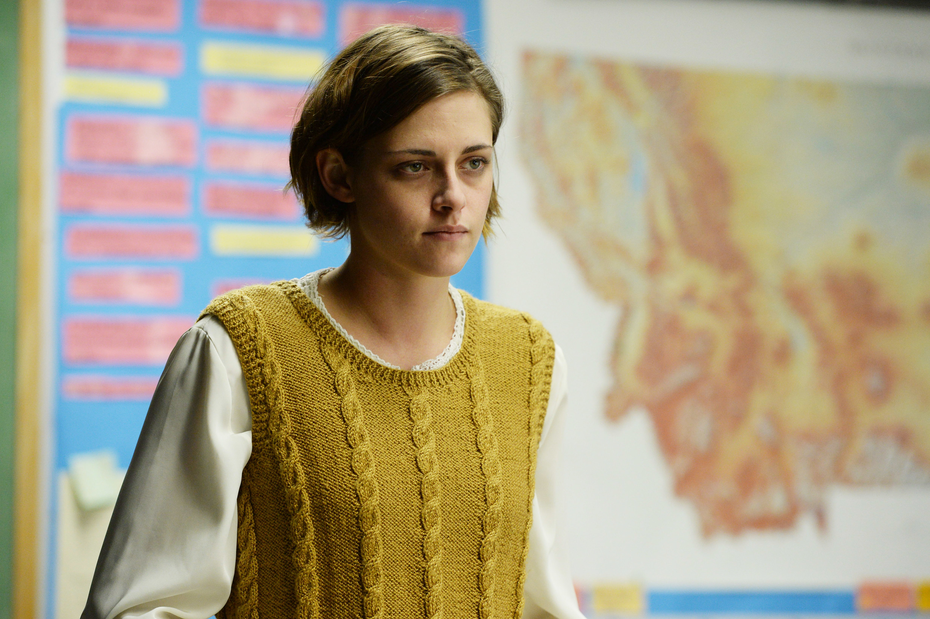 Kristen Stewart wearing a yellow vest in front of a map of Montana