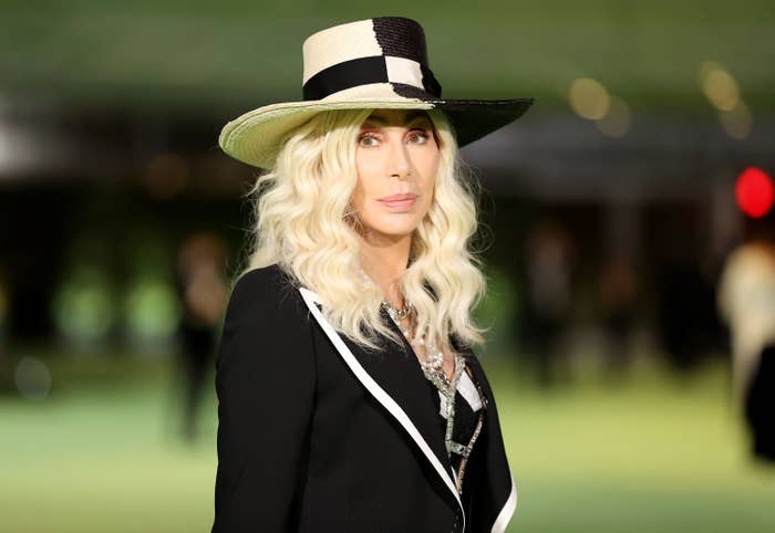 Cher poses for a photo while wearing a hat and a suit