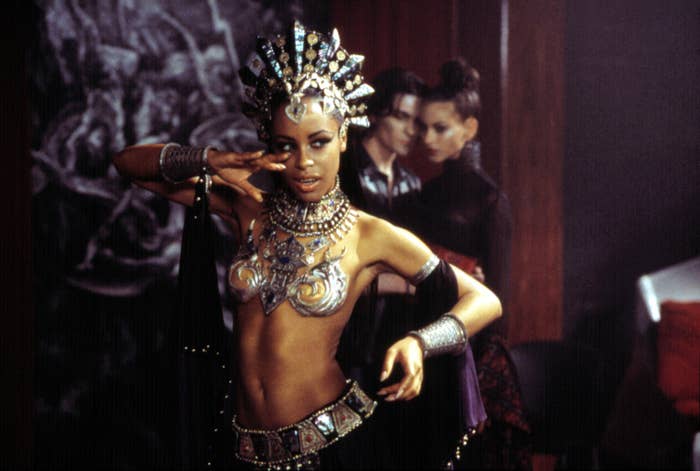 Aaliyah gestures with her hands while wearing a head piece and a breastplate