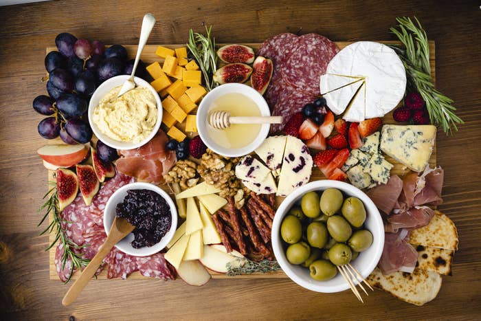 A board with assorted meats, cheeses, spreads, and fruits