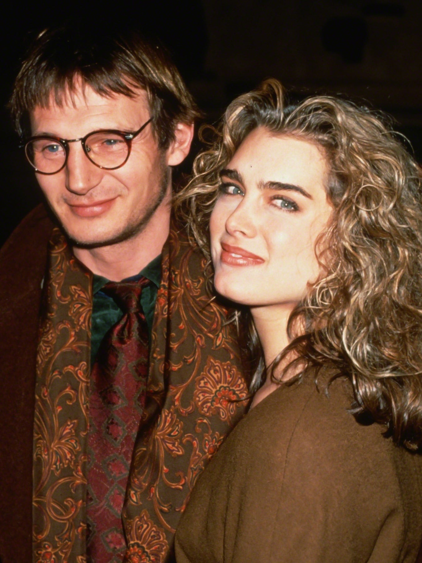 Photo of Brooke Shields and Liam Neeson smiling together in neutral outerwear