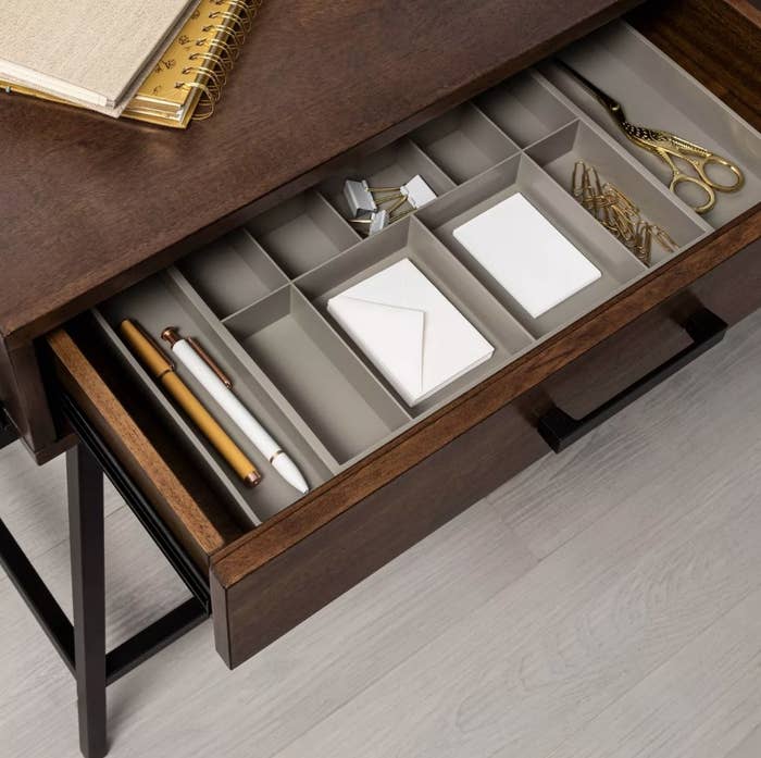 A grey expandable drawer organizer filled with pens and other office supplies