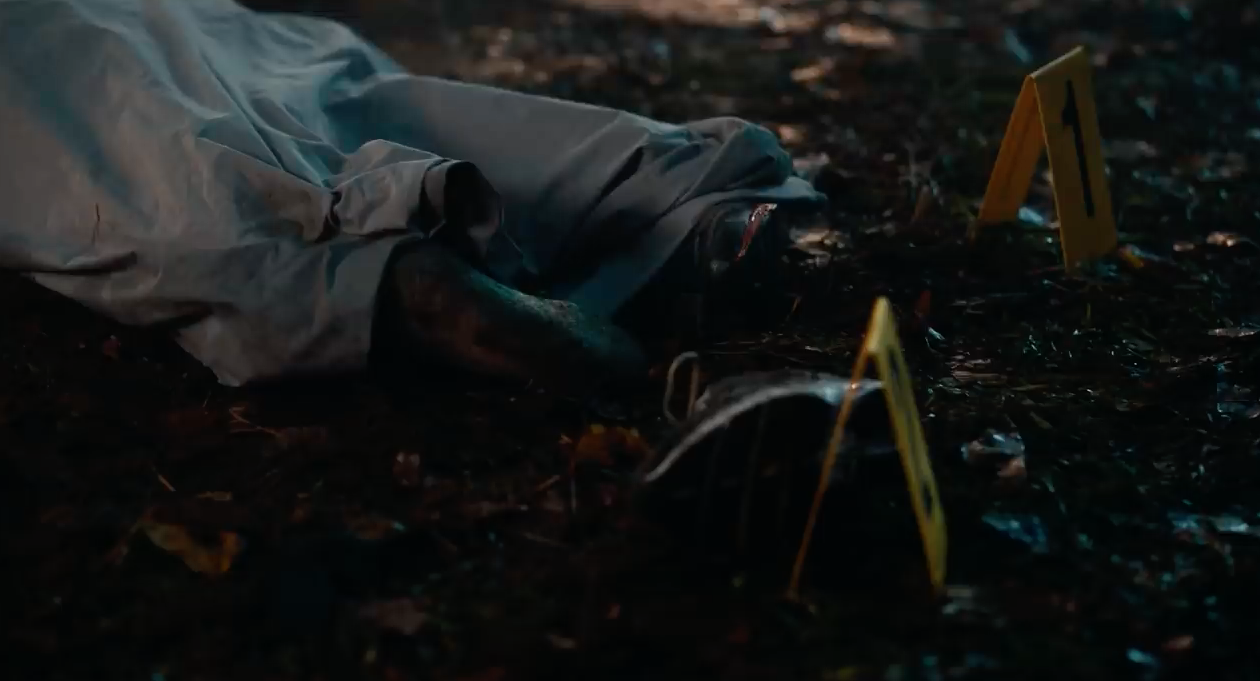A body under a tarp with a crime scene marker