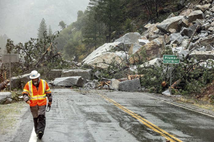 A man in high-vis clothing walks past the road covered in rocks.