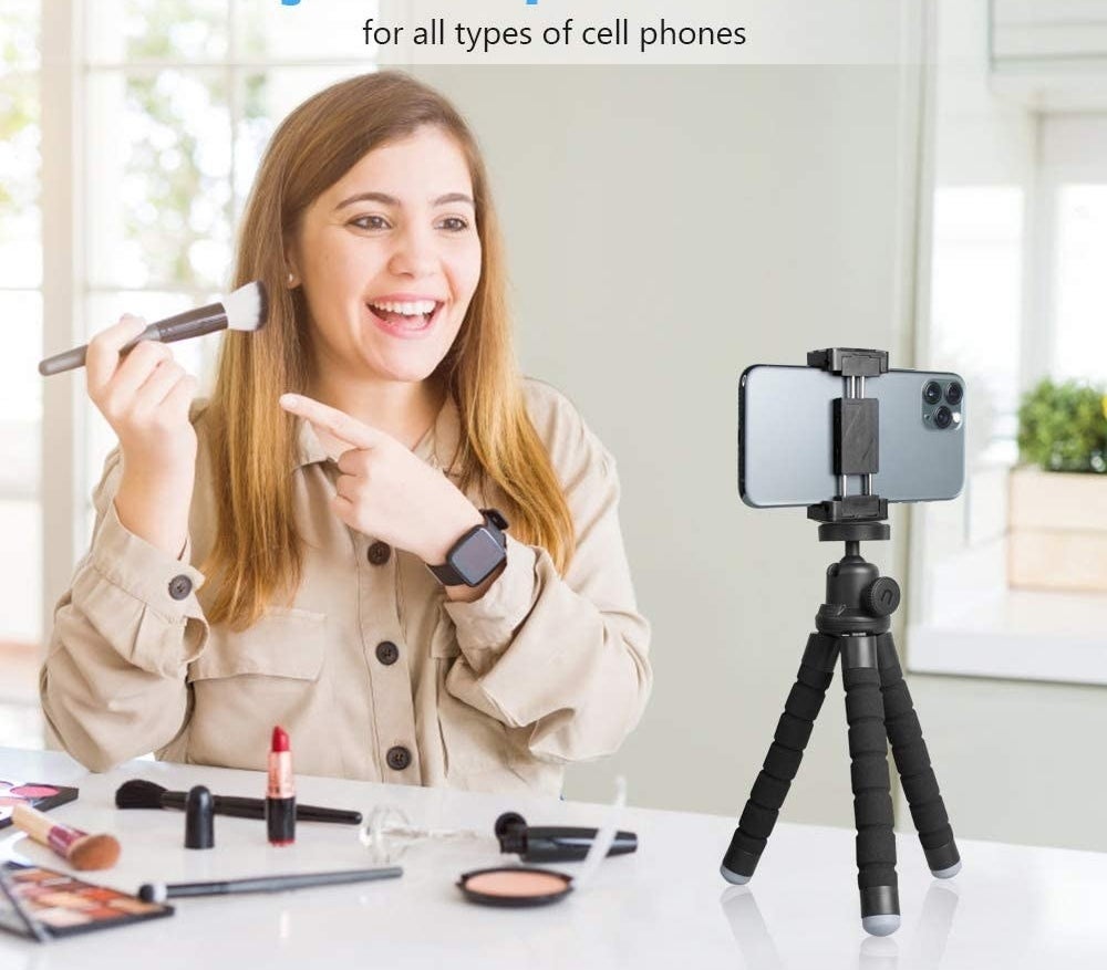 a person applying their makeup while their phone shoots a video; the phone is on the tripod