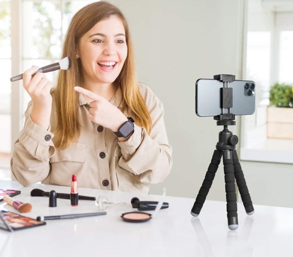 a person applying their makeup while their phone shoots a video; the phone is on the tripod