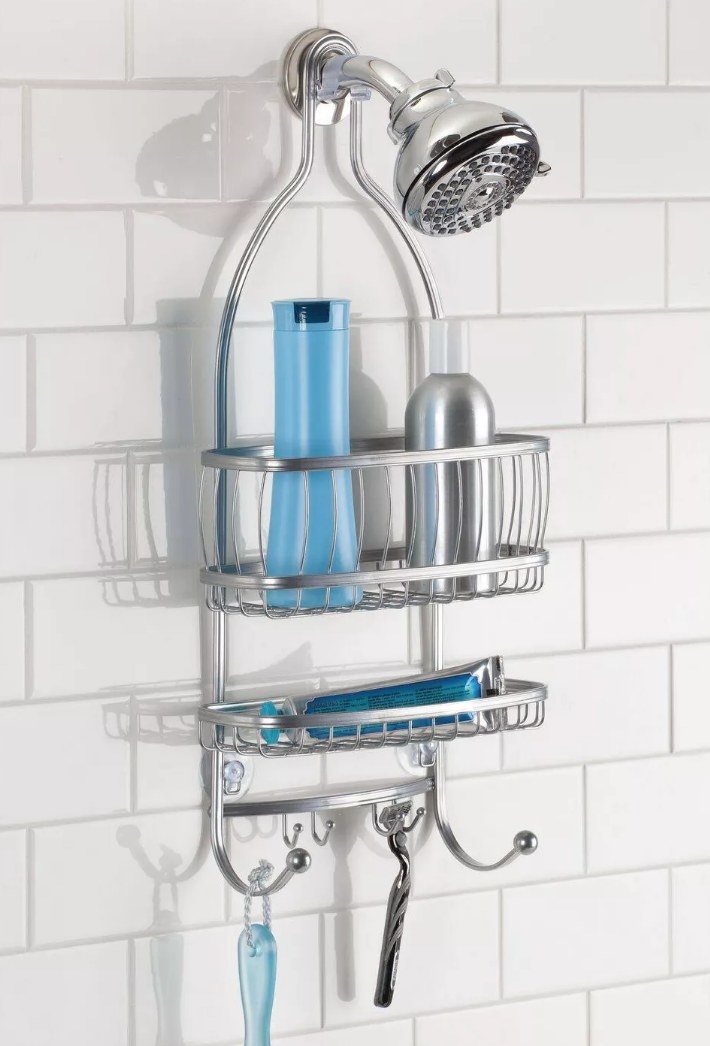 A silver shower caddy over a shower head with two shelves and six hooks