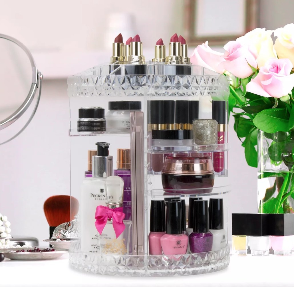 A clear, rotating makeup organizer filled with lipsticks, nail polish, and other products