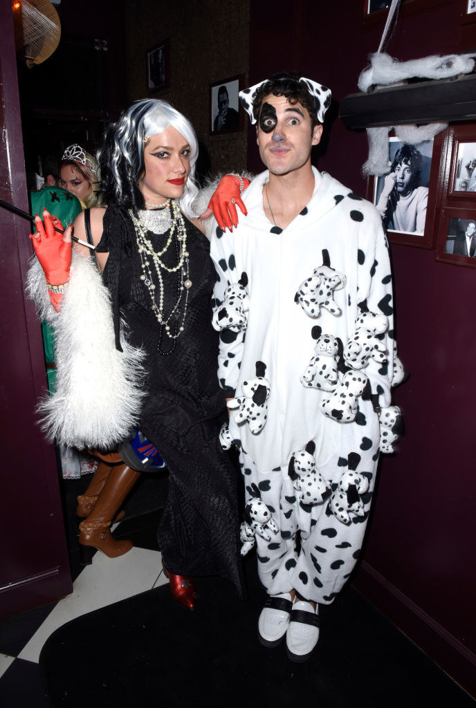 Mia Swier wears a dark dress with a fur shawl and Darren Criss wears a polka dot onesie with dog makeup on his face