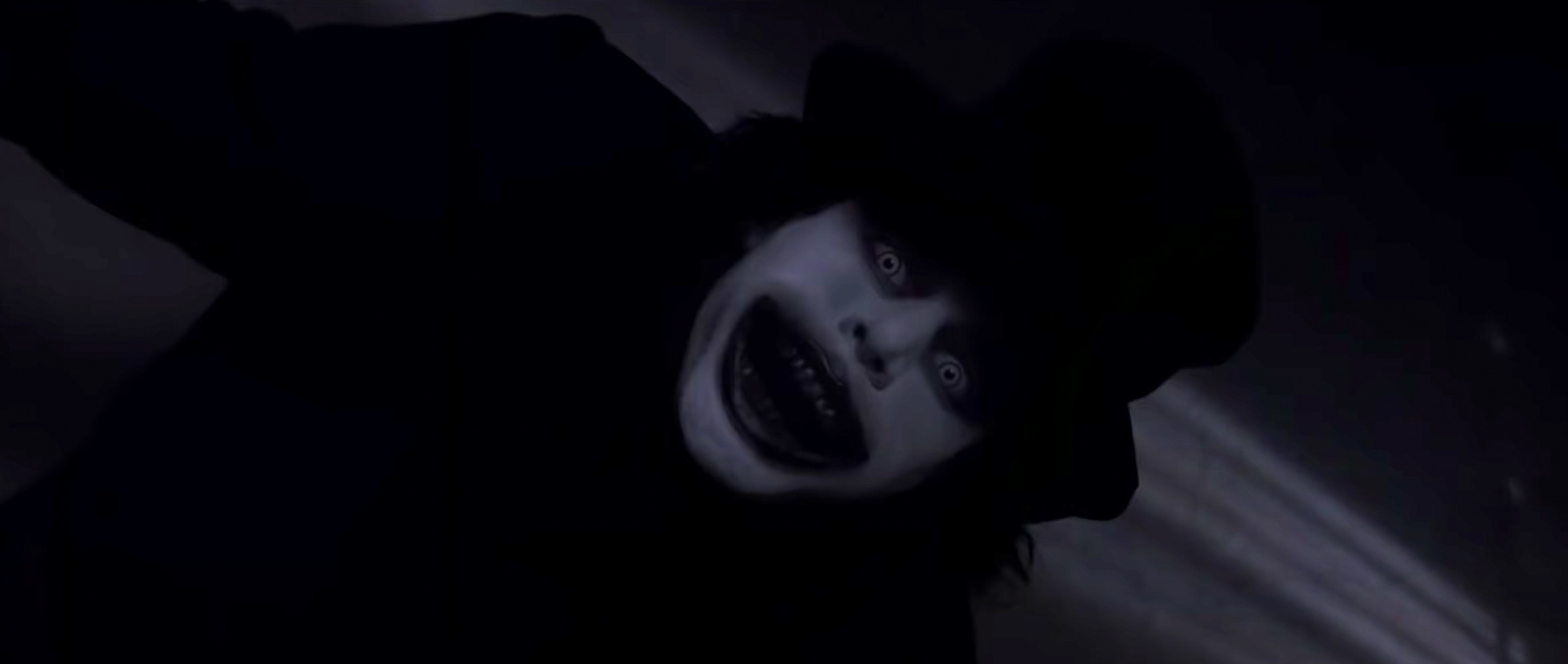 The Babadook, a dark figure in a top hat with a white face opens its mouth and widens its eerie-looking eyes