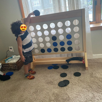 Reviewer's photo of their child dropping a black disc into the wooden hole