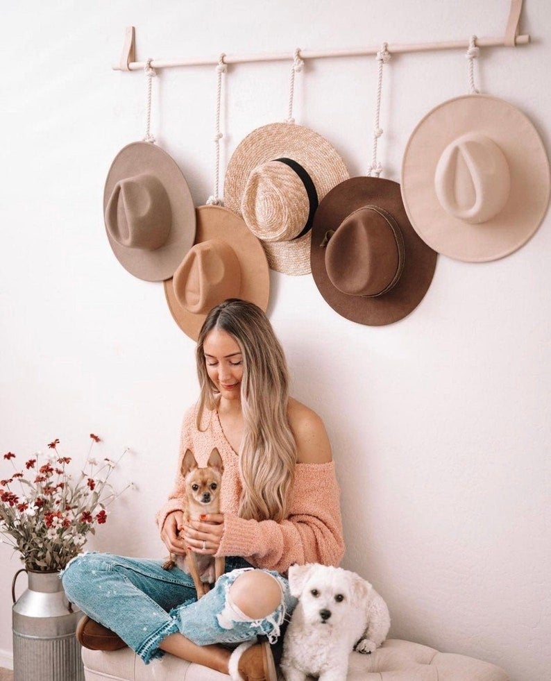A model and two dogs sitting below the hat hanging rack, which is hanging five wide-brimmed hats