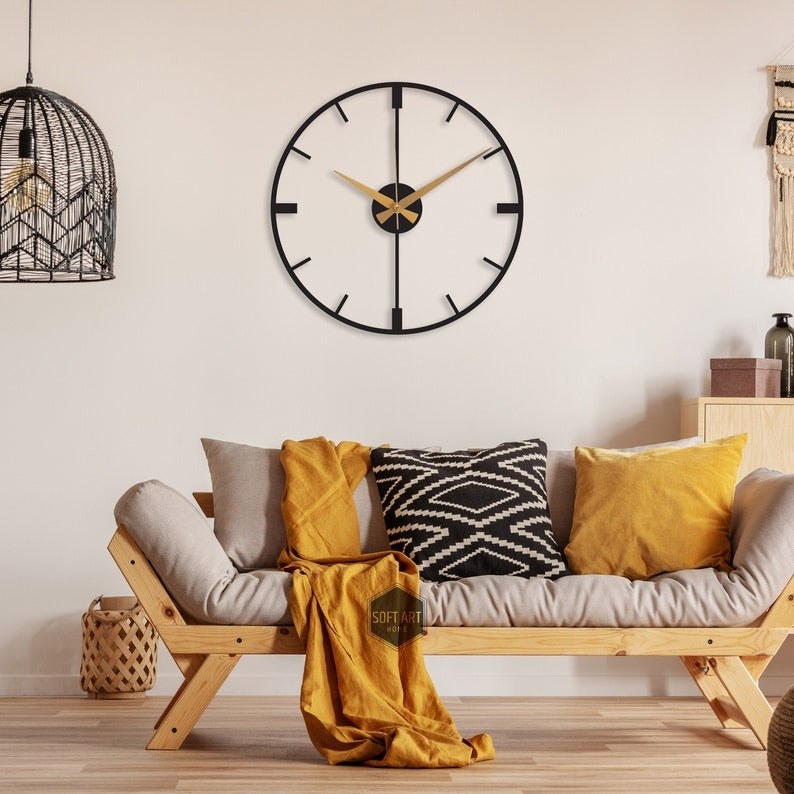 a black minimalist clock with gold arms on a wall in a room with a futon-style couch