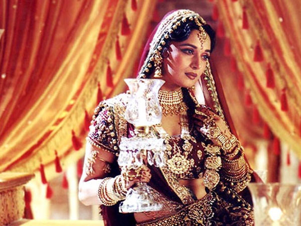 Bollywood actress Madhuri Dixit dressed in traditional red attire, with a candle holder in one hand, playing Chandramukhi for the movie Devdas.