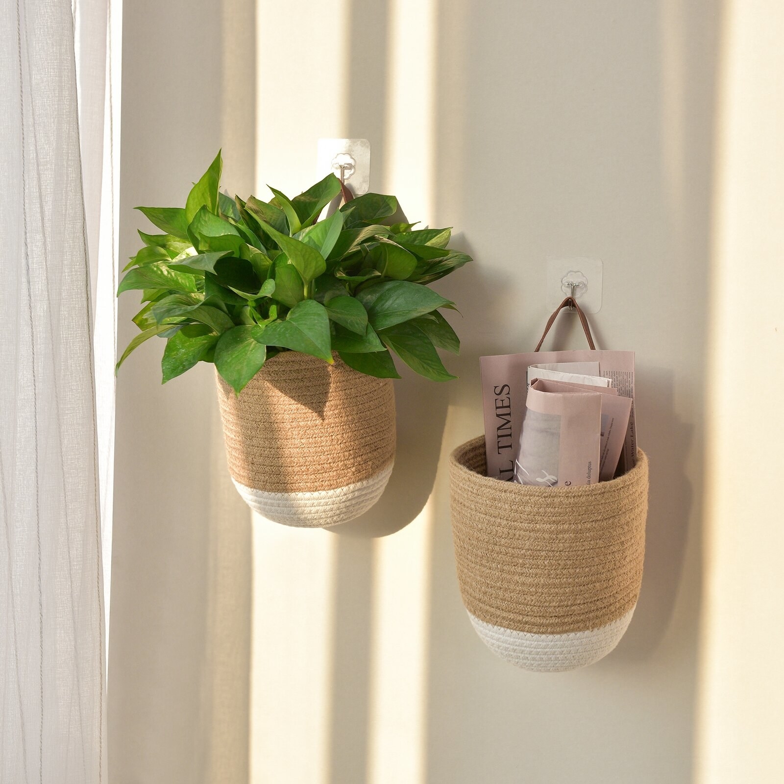 two jute baskets hanging on two hooks, one filled with newspapers and the other with a healthy Pothos plant. Each basket is a natural color with a white bottom