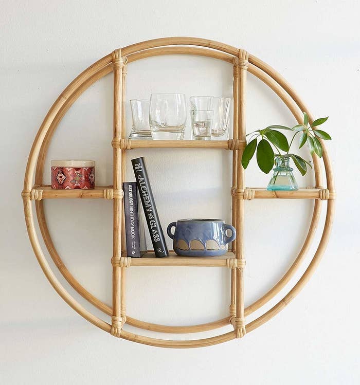 A circular rattan shelf with books, plants and ceramics on it