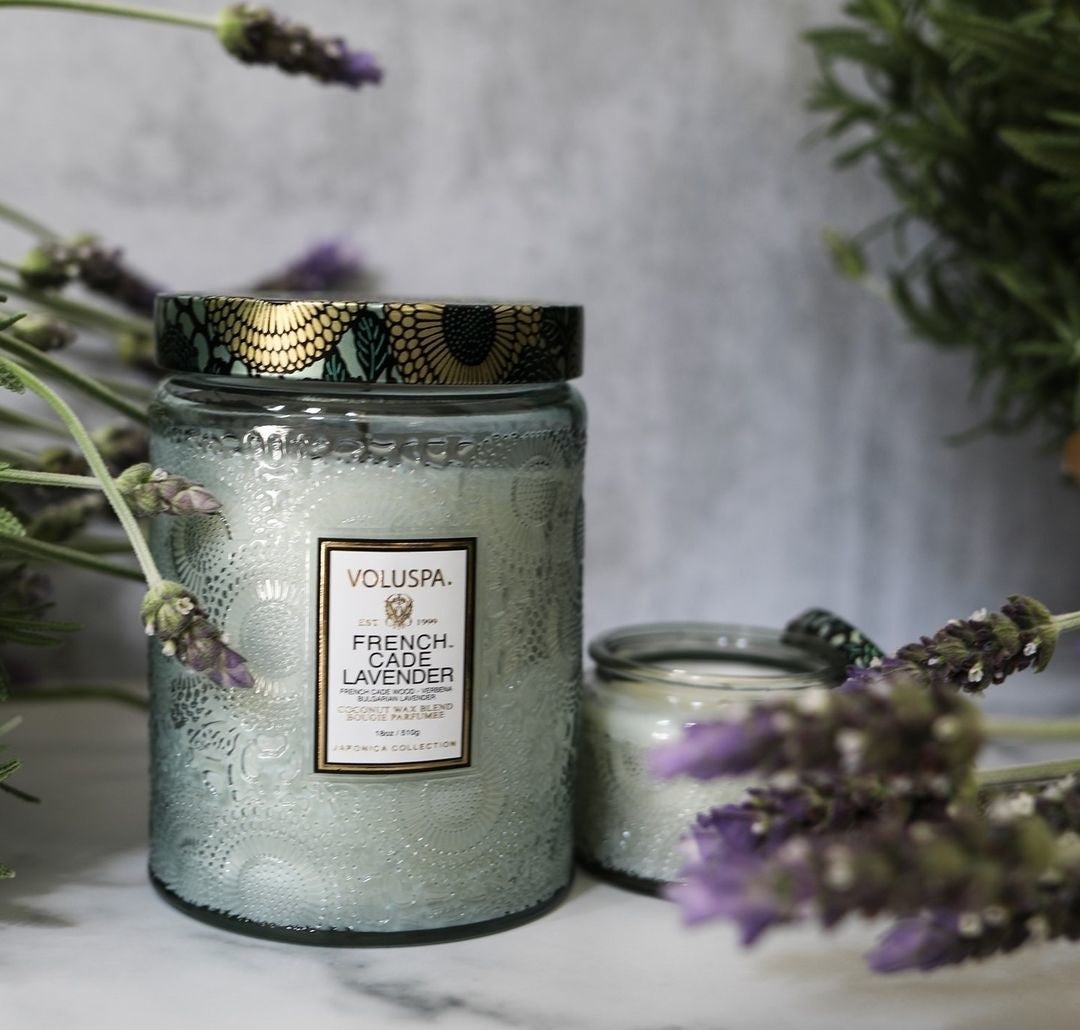 a lavender scented candle on a marble counter surrounded by lavender boughs